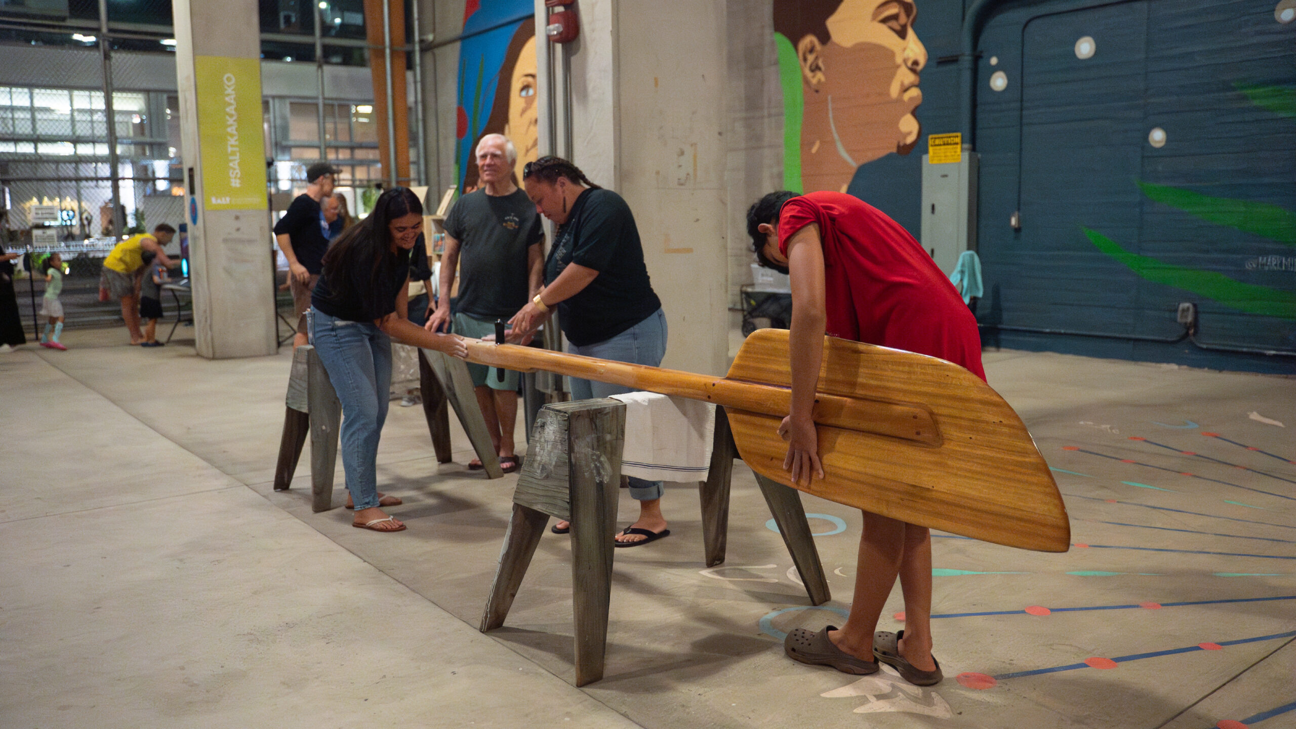 A group of visitors sand a large wooden paddle